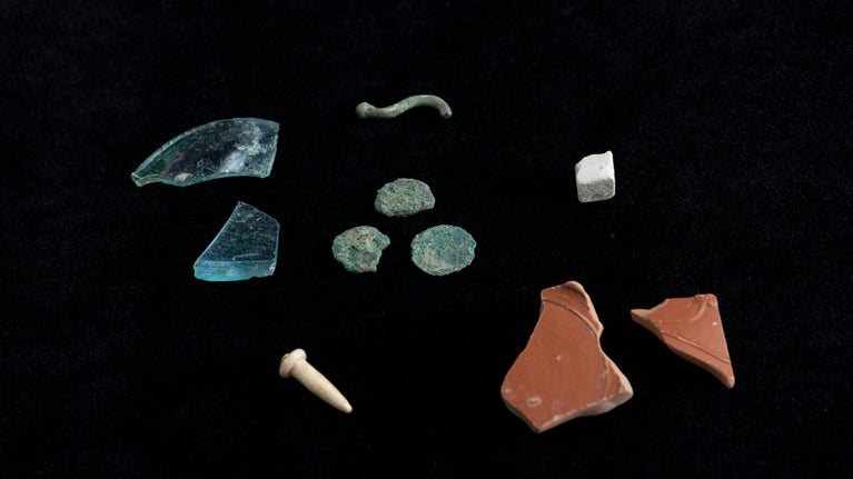 Fragments of ceramic, stone and glass Roman artefacts against a black background.